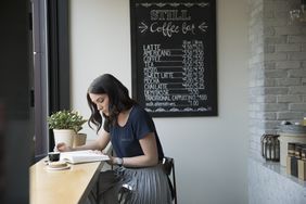 Woman reading book in café with chalkboard menu in background