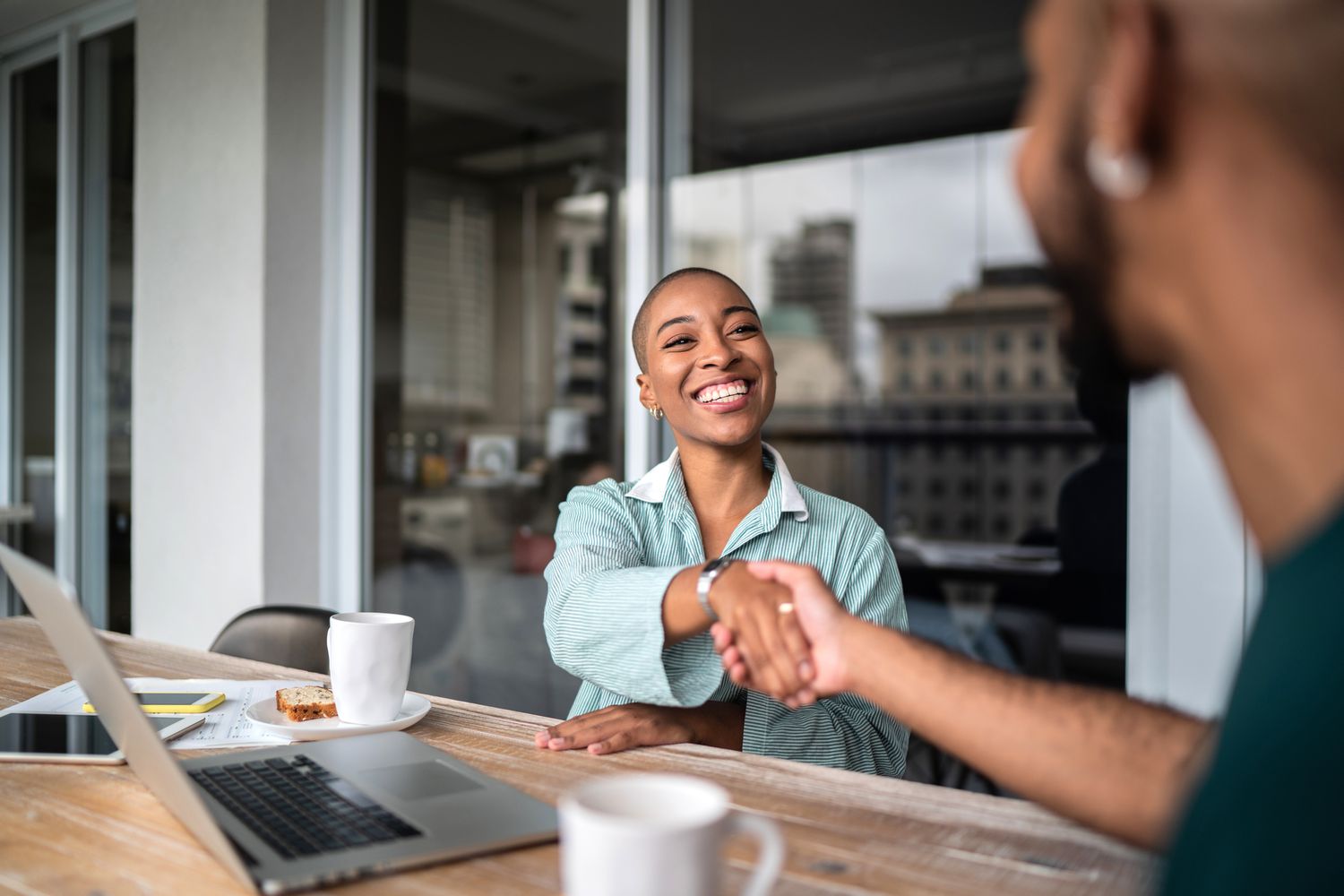 Two people sitting at a desk shake hands.