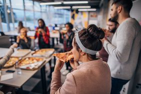 Group of coworkers eating pizza in a break room with some sitting and some standing