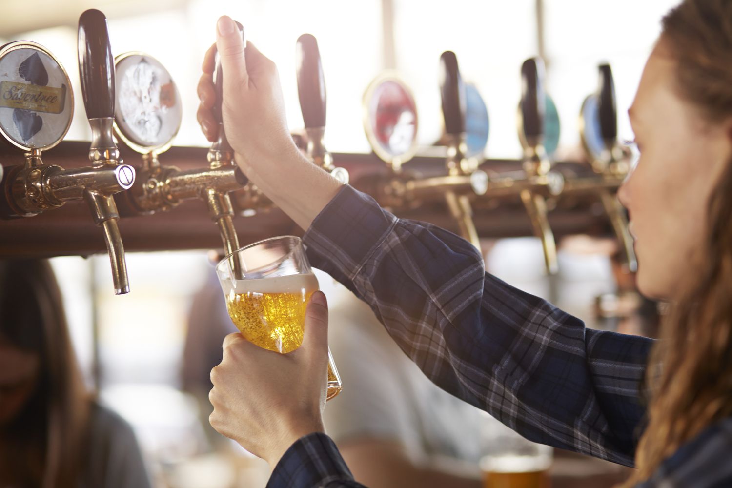 A woman fills a glass with beer at the tap. 