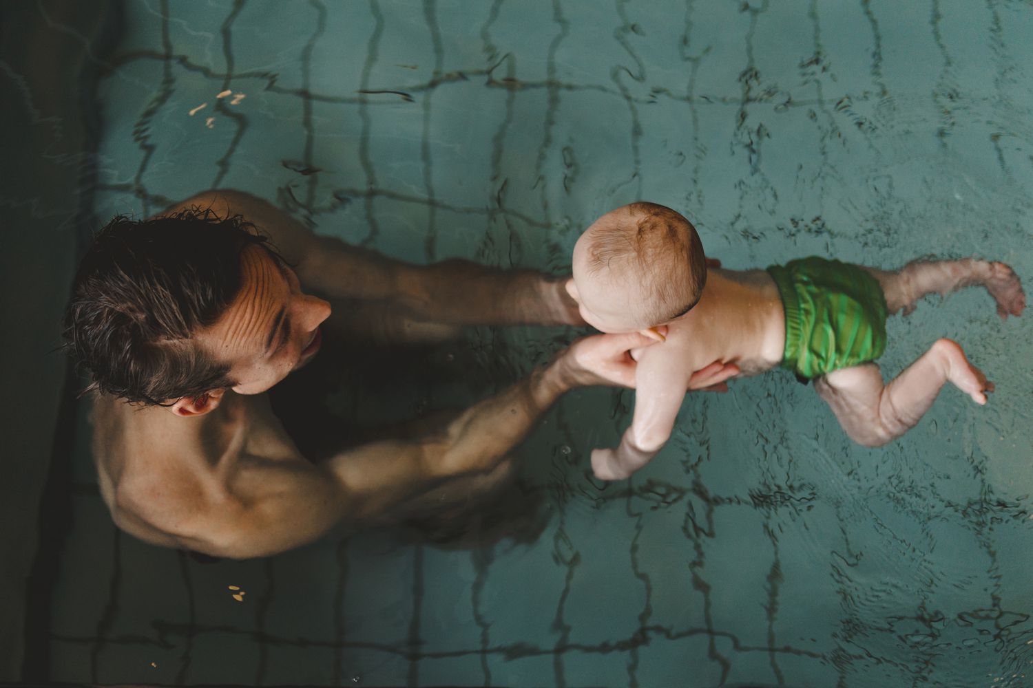 Dad in a pool with an infant in a swim diaper