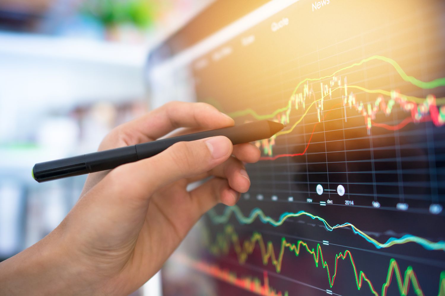 Hand holding a stylus writing on a computer monitor displaying charts.