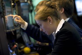 A female trader is pointing to a screen while looking down.