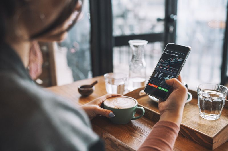 A person using a smartphone to check investments at a coffee shop.