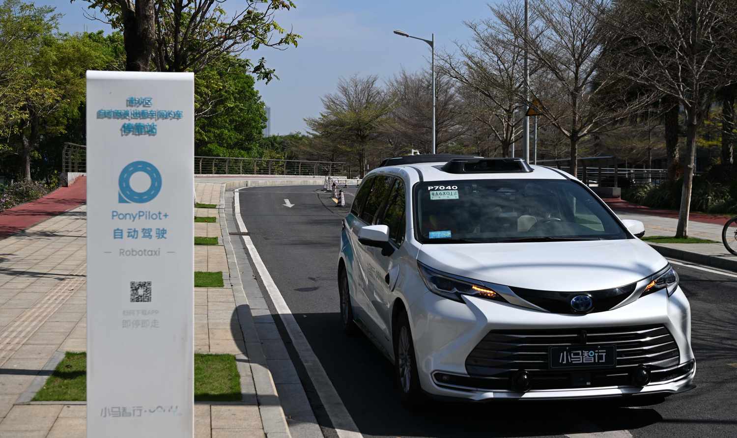 A white minivan robotaxi made by Pony AI drives by a sign that says PonyPilot