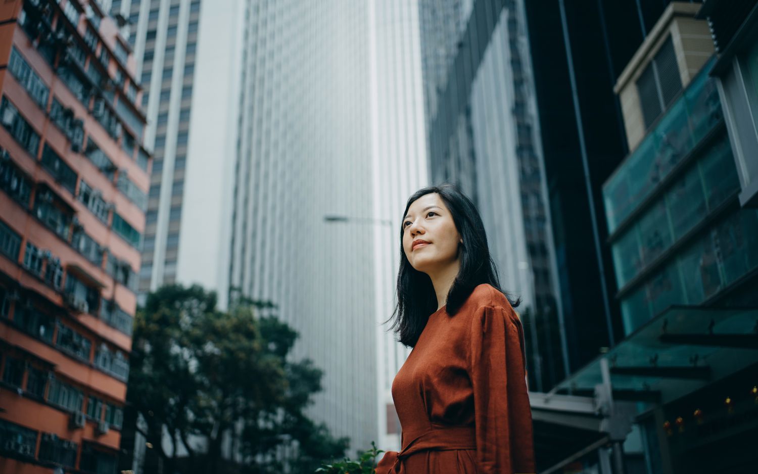 Low-angle portrait of a confident young woman standing against high-rise buildings in a city.