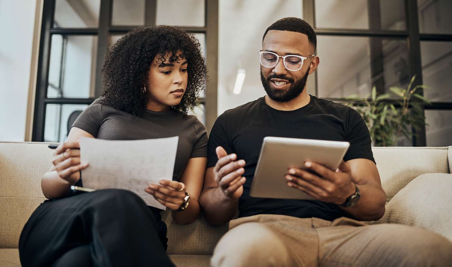 Young couple on a couch looking at a tablet and paperwork