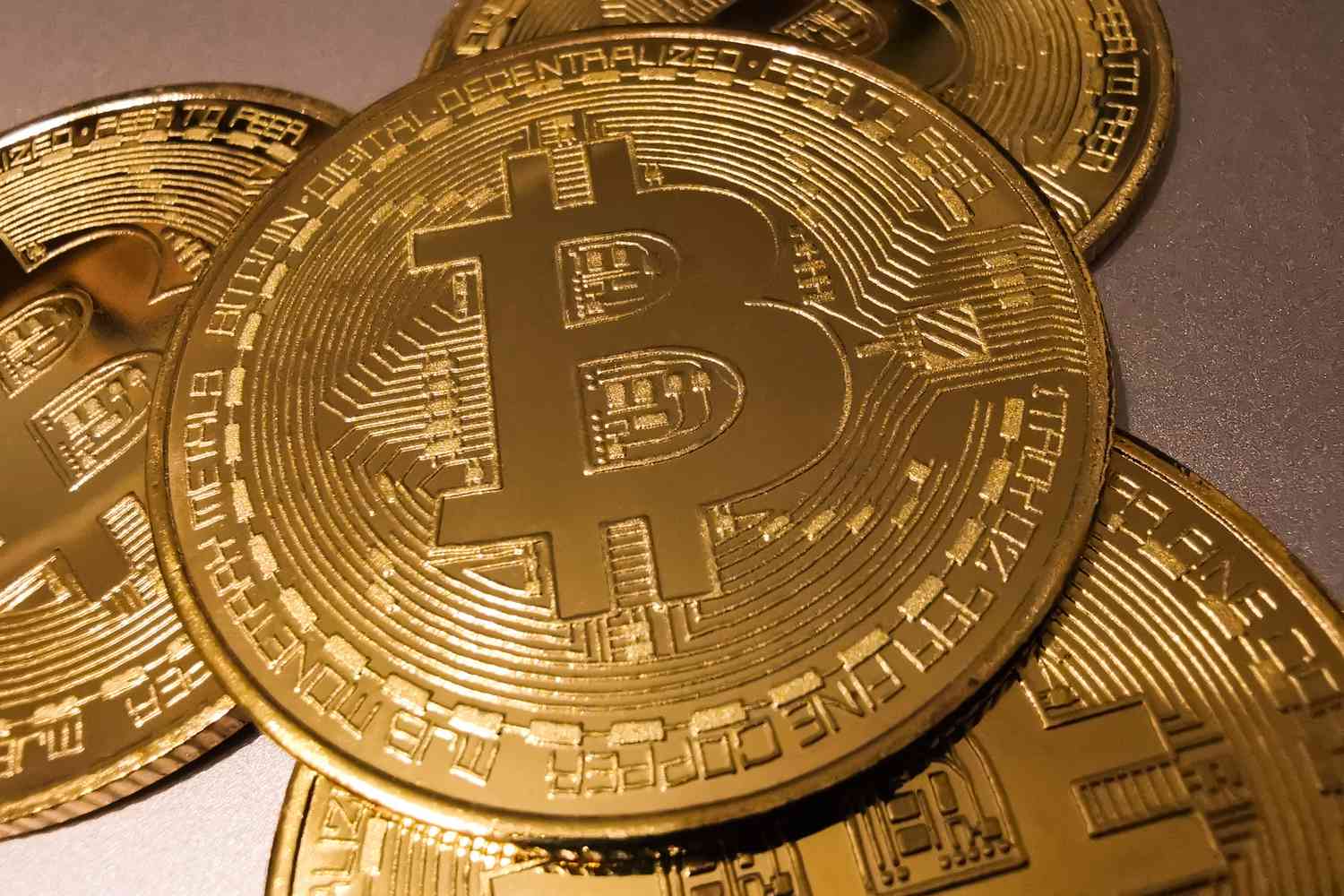 A stack of gold coins with the Bitcoin "B" symbol sit on a table.