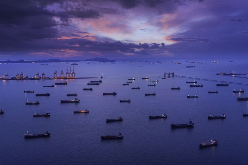 Aerial view Oil ship tanker park on the sea at dusk with beautiful sky waiting for load/unload oil from refinery for transportation.