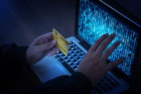 Hands of anonymous hacker holding credit card in front of a laptop