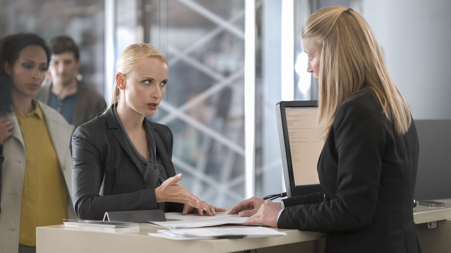 A woman speaking with a bank teller, others waiting in the background
