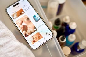 A smartphone displays skincare information on the Hers app, with cosmetic products visible nearby