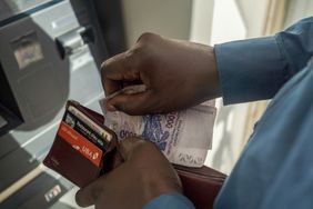 A bank customer withdraws West African Franc banknotes from an automated teller machine.