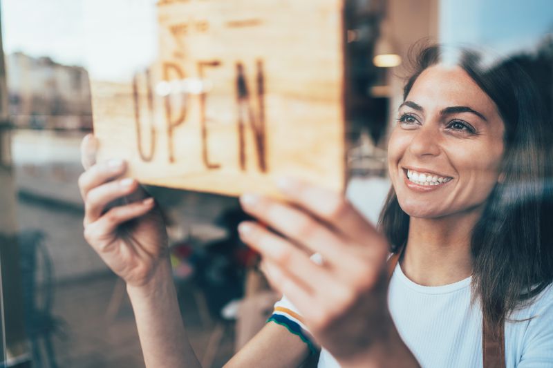 Happy business owner hanging an open sign on the door at a cafe