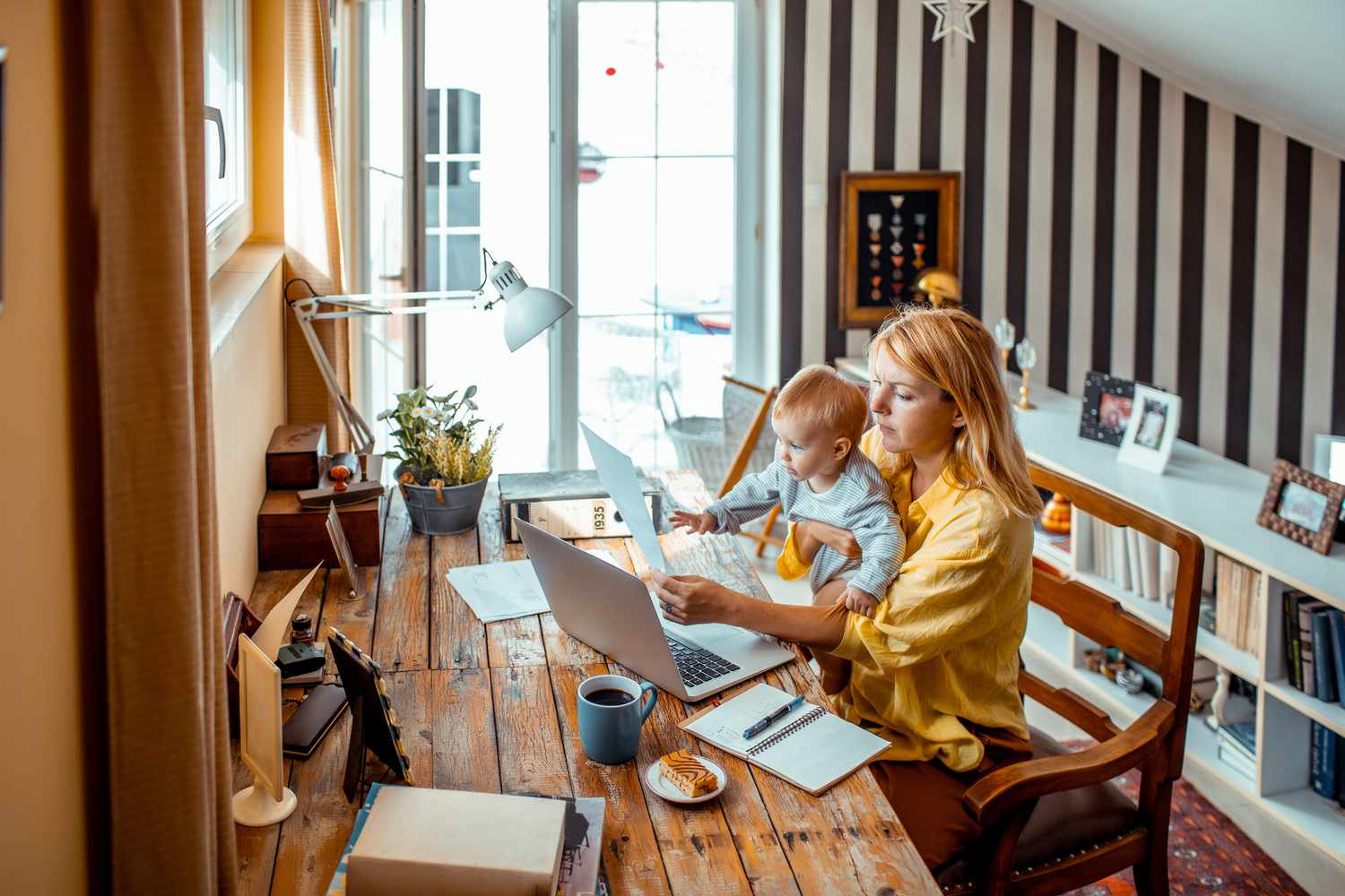 Young mother working from home sitting at a table holding her child in her lap