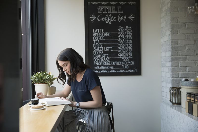 Woman reading book in café with chalkboard menu in background