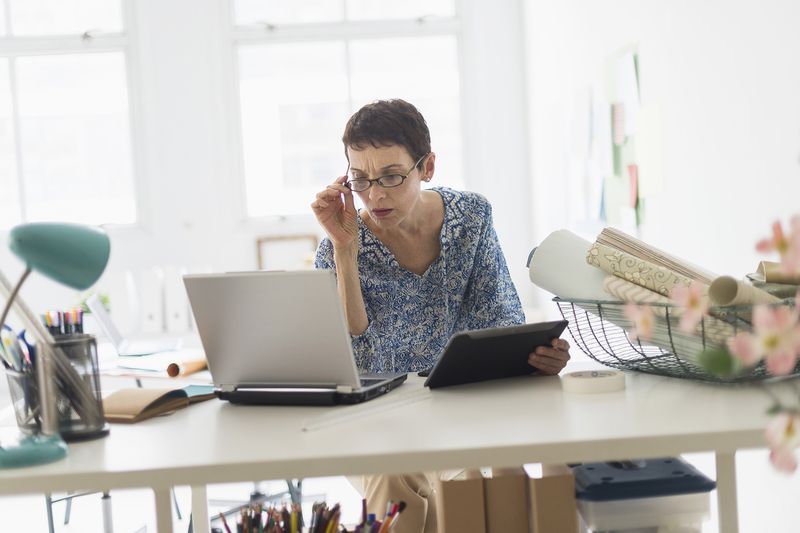 Senior Business Woman Using Laptop and Tablet in Office