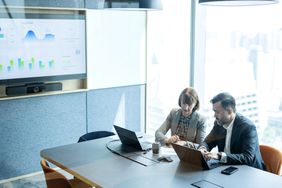 People working in a conference room with charts on a wall screen
