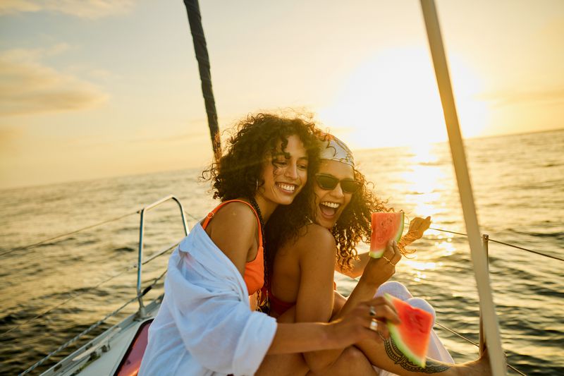 Two individuals on a boat at sunset holding watermelon slices, smiling and enjoying the moment