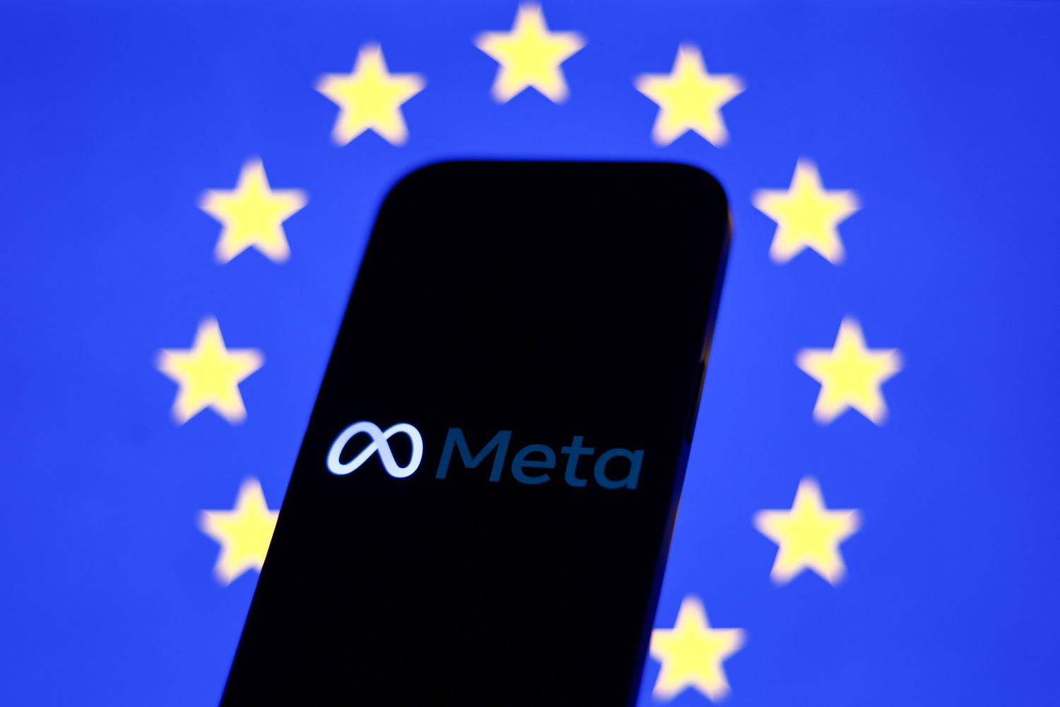 The Meta logo is seen on a phone screen in front of a European Union flag.