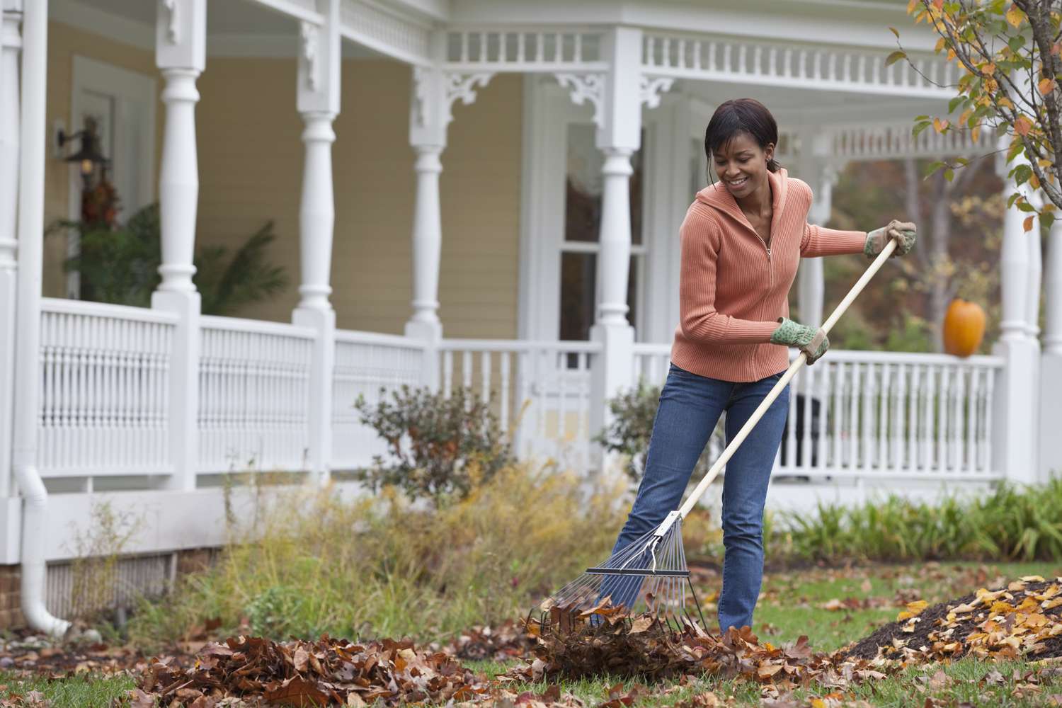 A woman raking leaves in front of her house