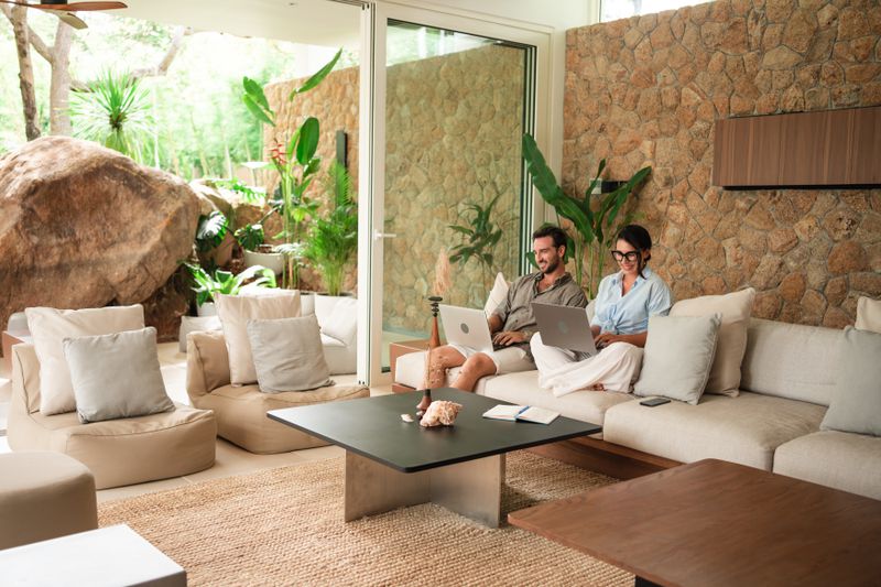 A couple works on their laptops while sitting next to each other on a couch inside of a luxury vacation home.