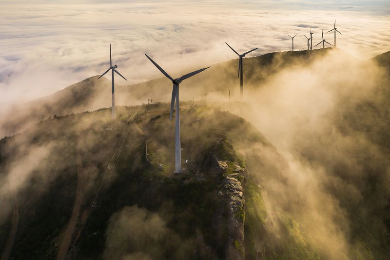 wind turbines on top of a mountain with cloud cover at sunset