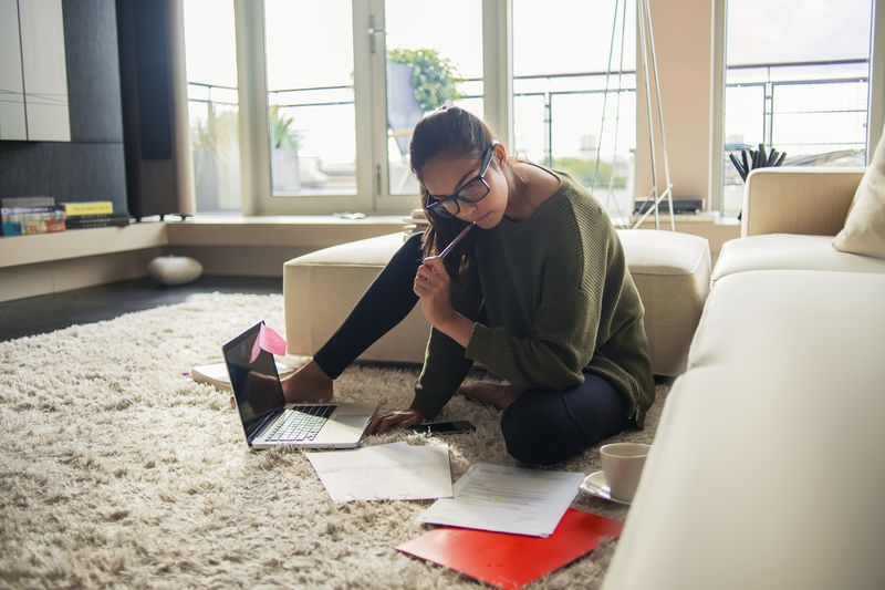 woman sits on carpeted floor with laptop considering personal loan options