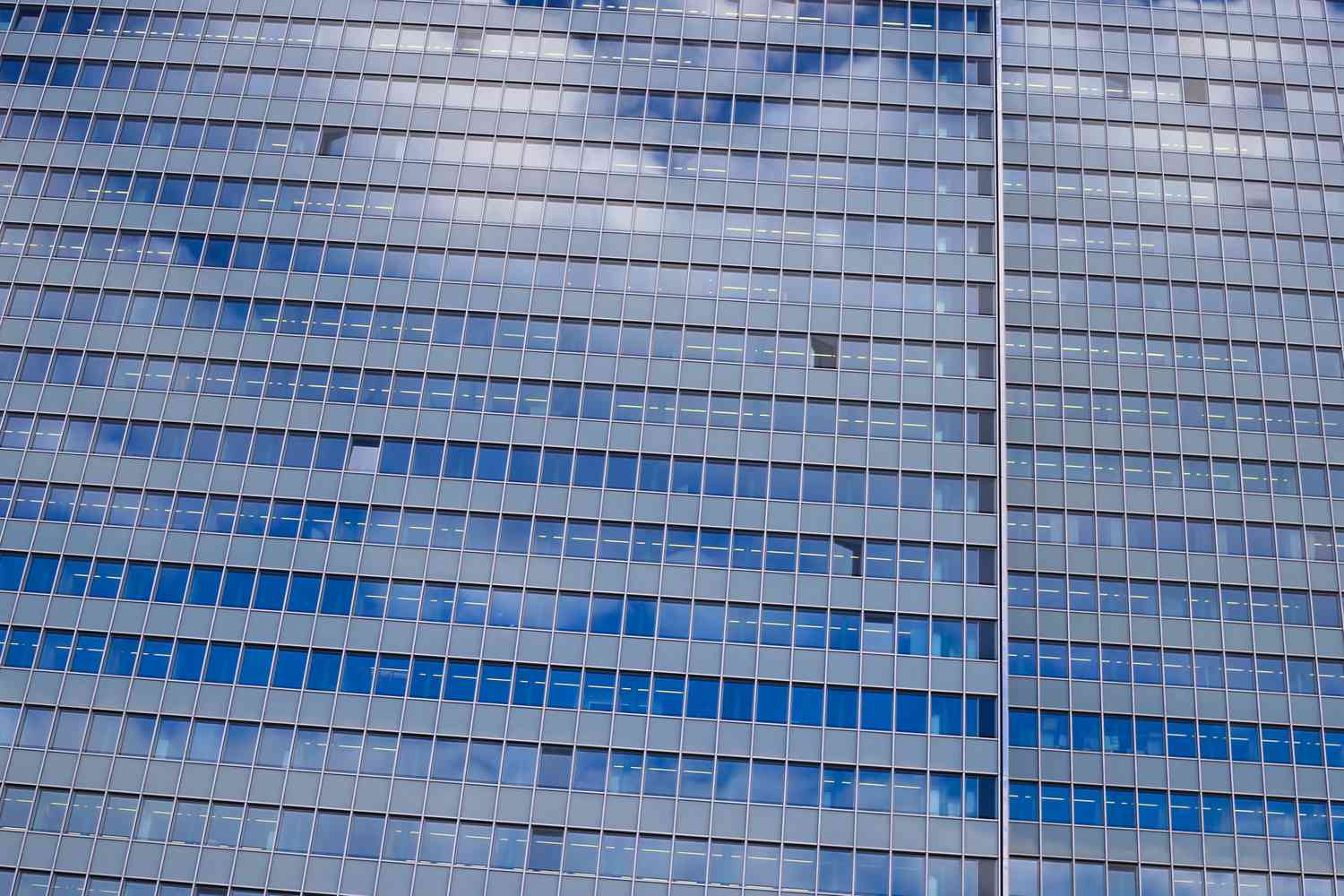 View of a facade of skyscraper with countless windows and reflection of clouds and sky.