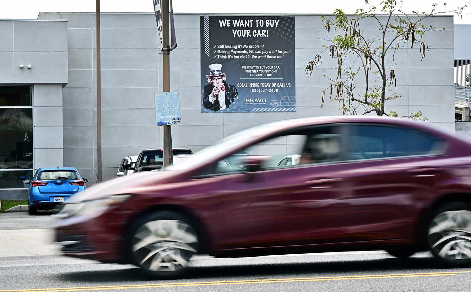 A car drives past a sign at an auto dealership selling used cars on April 28, 2025 in Alhambra, California.