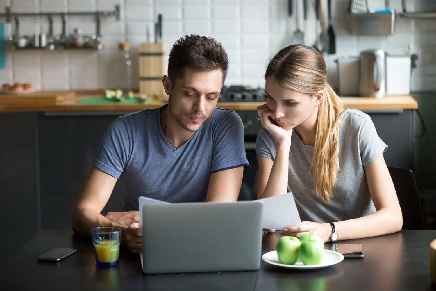 Young couple sitting in their kitchen and looking at mortgage documents and a laptop