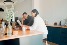 Couple in their 30s sitting in their kitchen and looking at mortgage documents and a laptop