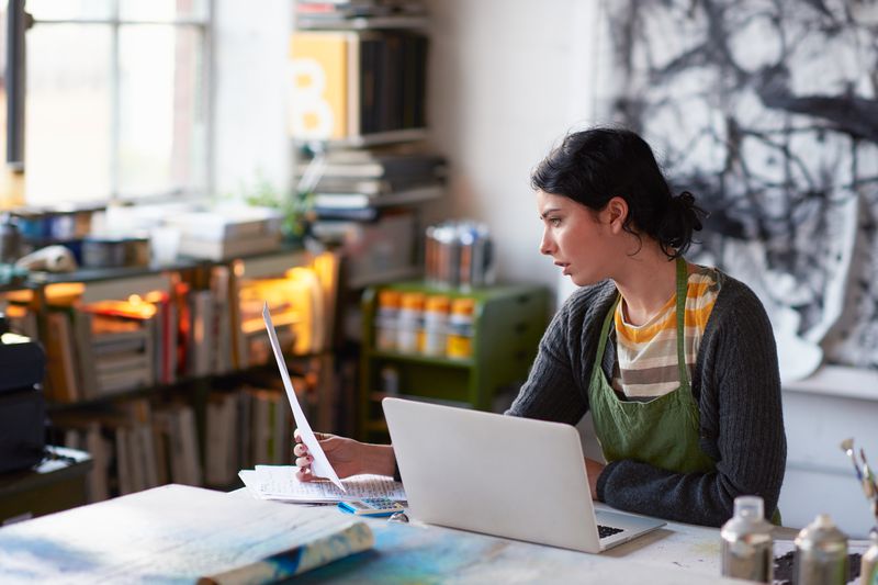 Young female artist in studio working on laptop.