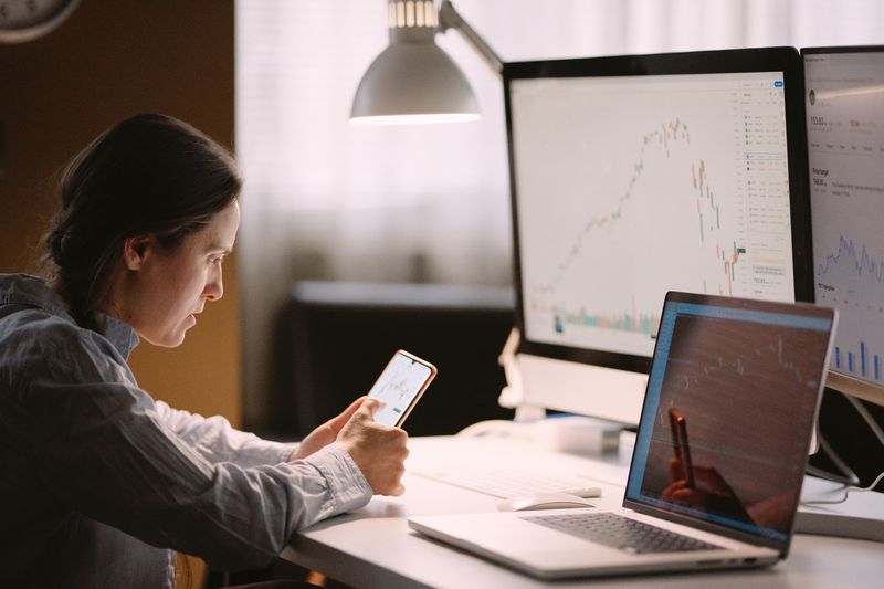 Woman studying stock markets on TradingView app, checking on trading positions and stock markets in the evening at home.