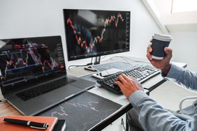 An investor reviews stock charts on a laptop and monitor.