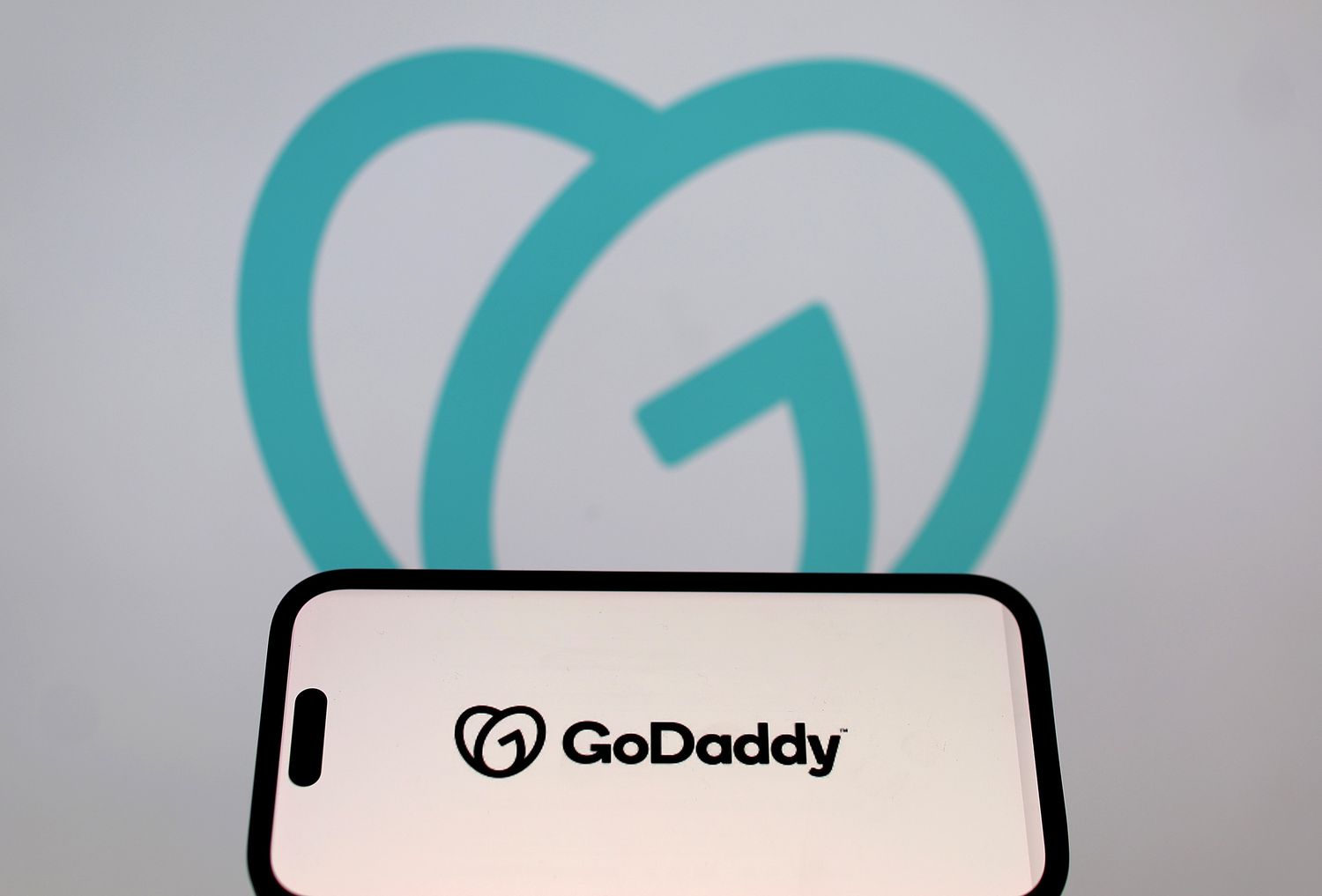 The GoDaddy logo is displayed on an iPhone screen in front of a screen with the company logo on April 4, 2024 in San Anselmo, California. 