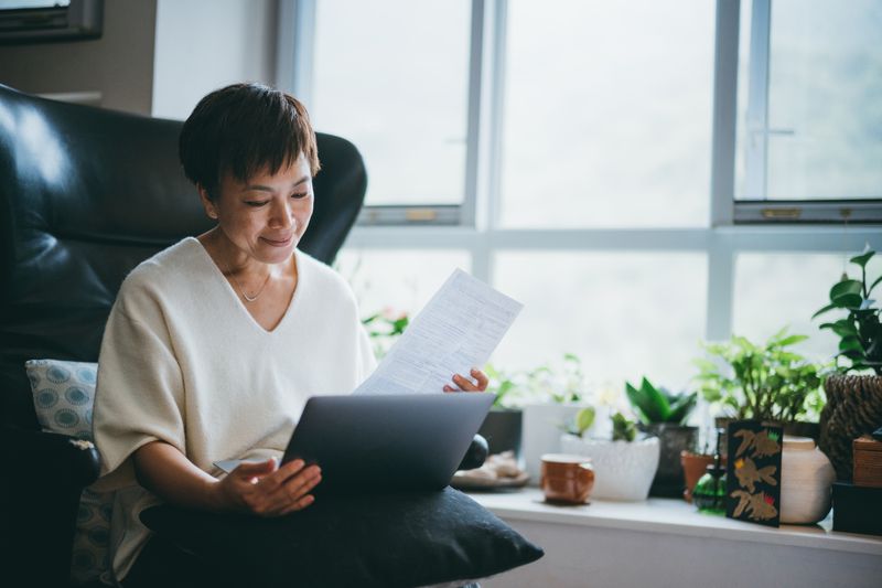 Woman reviewing paperwork with a laptop at home