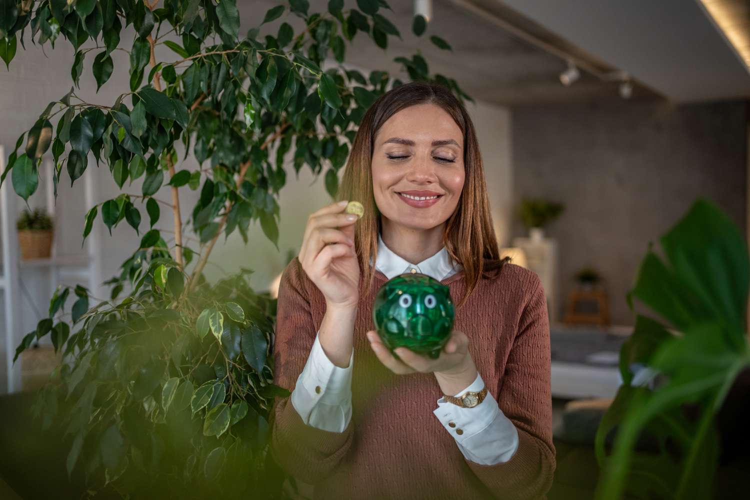 A person closing their eyes putting a coin in a green piggy bank.