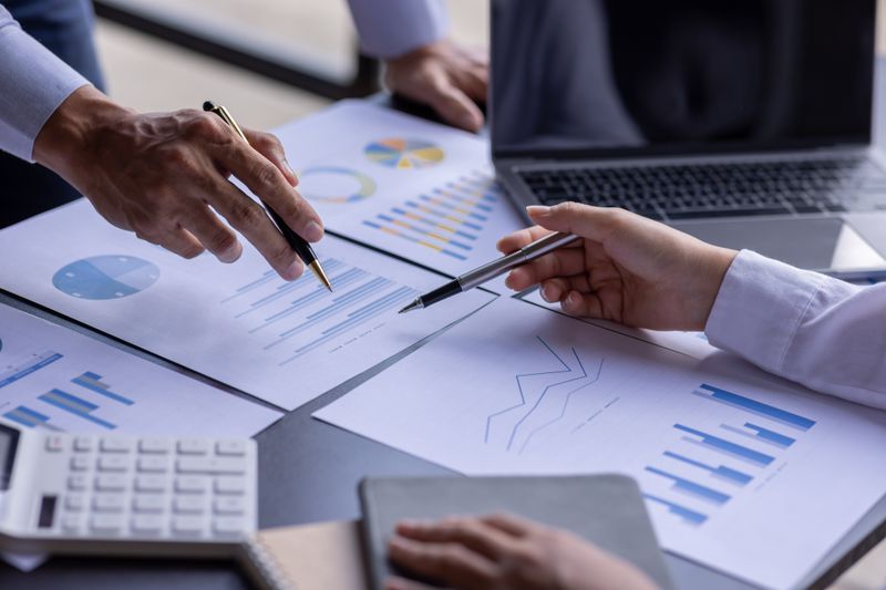 An accountant team are analyzing data charts pointing pens at paper charts.