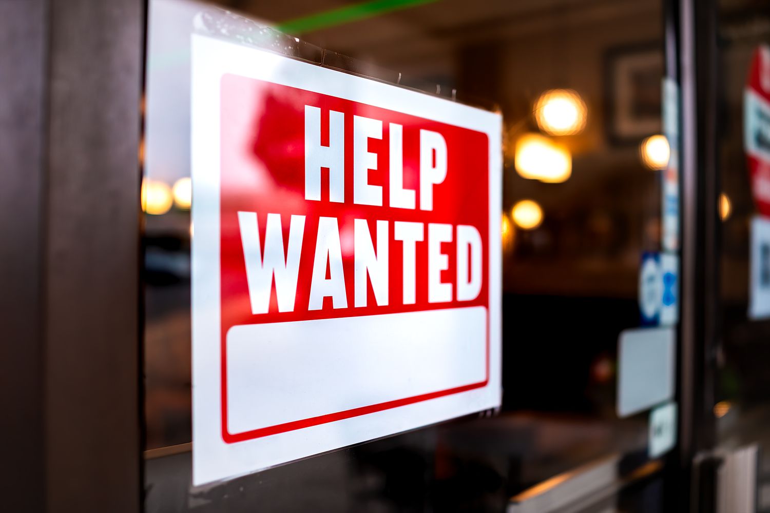 Sign text closeup for help wanted with red and white colors by entrance to store shop business building 