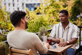 Young gay couple talking over coffee on their apartment balcony
