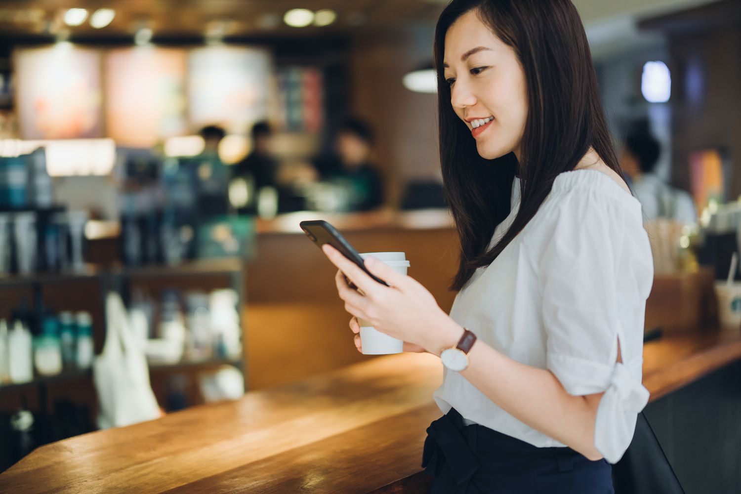 Young woman checking mobile phone while standing at counter in coffee shop