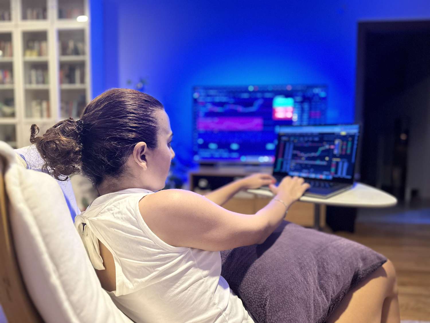 Female trader sitting on a low chair with a cushion on her lap working on a laptop.