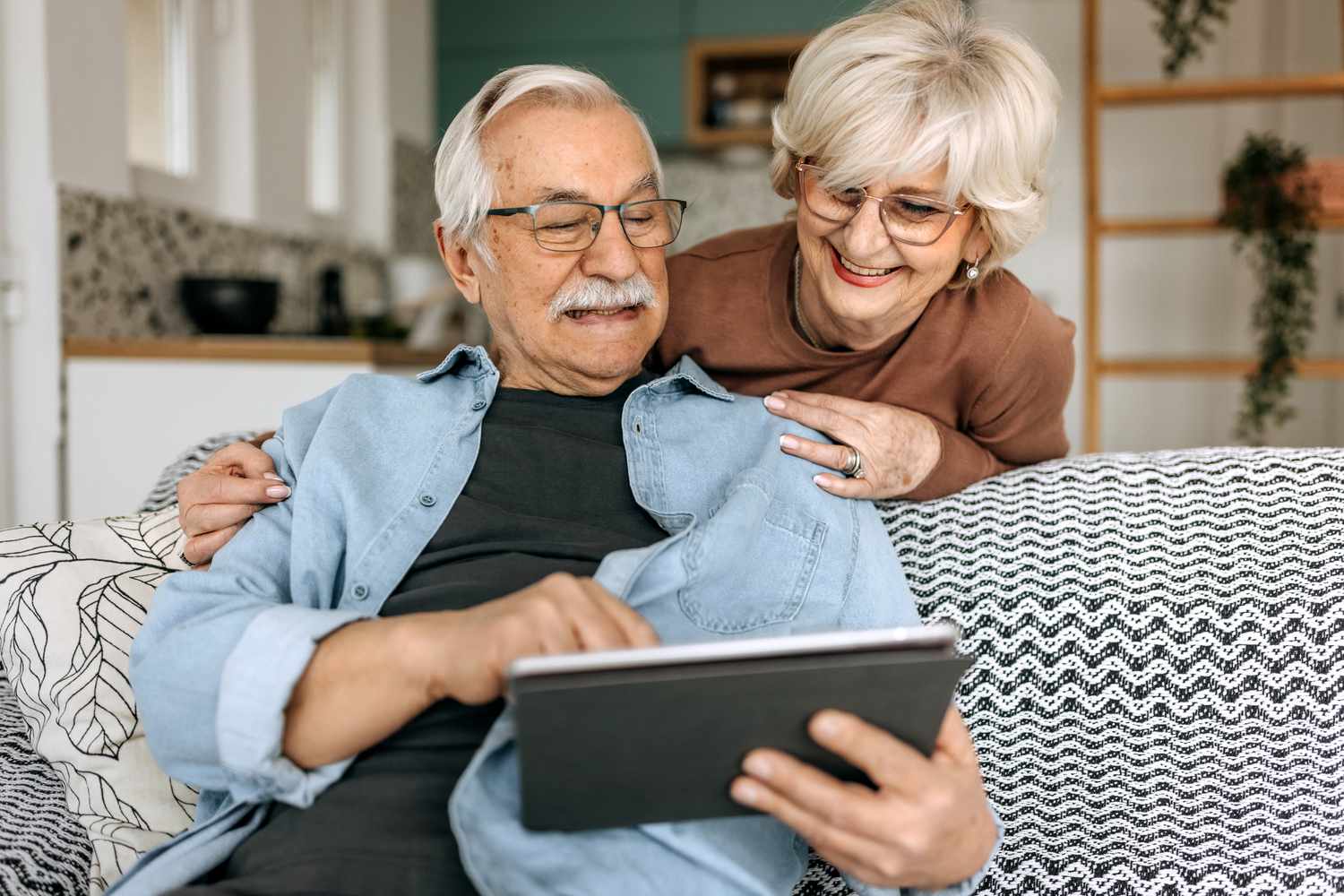 A man and a woman sit and lean on a couch looking at a tablet computer