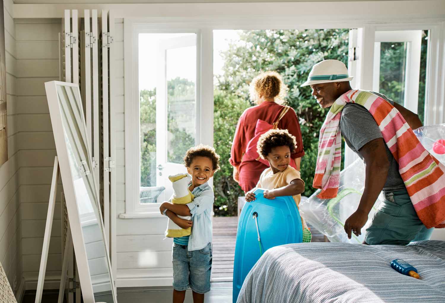Father, mother and two sons excited to head out on a holiday or vacation getaway. Sibling brothers and their parents with towels and toys for an outing. 