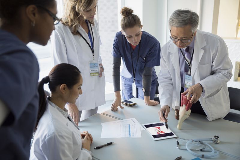 Doctors with model using digital tablet in meeting.