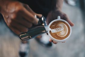 A hand pouring cream into a cup of coffee