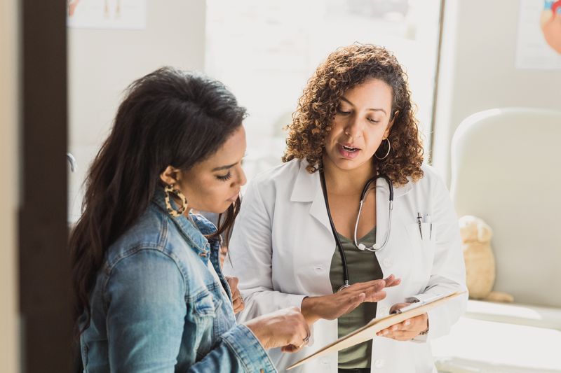a doctor discusses a medical chart with a woman in a denim jacket