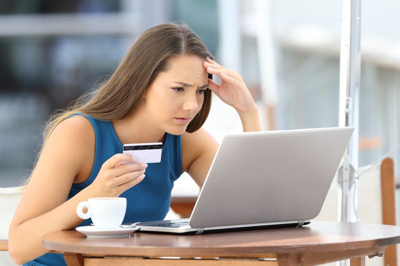 A worried woman looks at her laptop while holding a credit card.