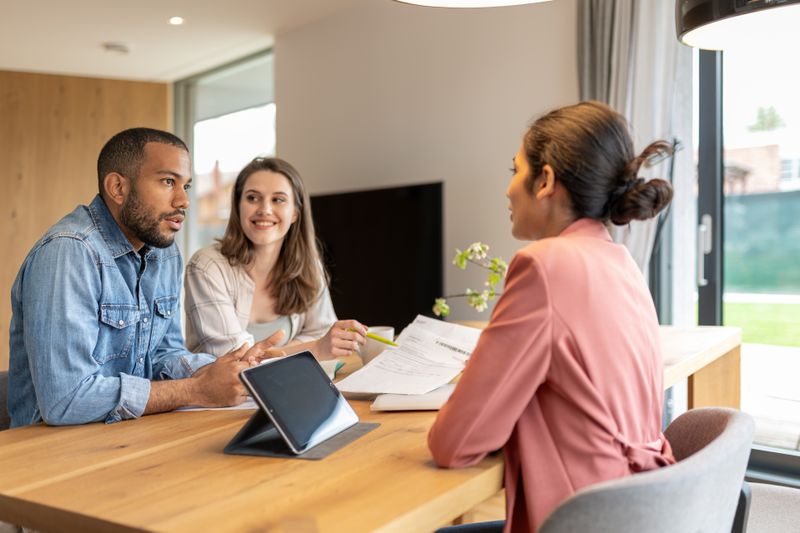 An Indian financial advisor advises a multiracial couple in their apartment about a financial investment.